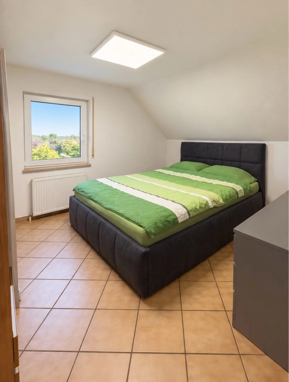 Eingerichtetes Schlafzimmer mit Fenster, Fliesenboden und leichter Dachschräge