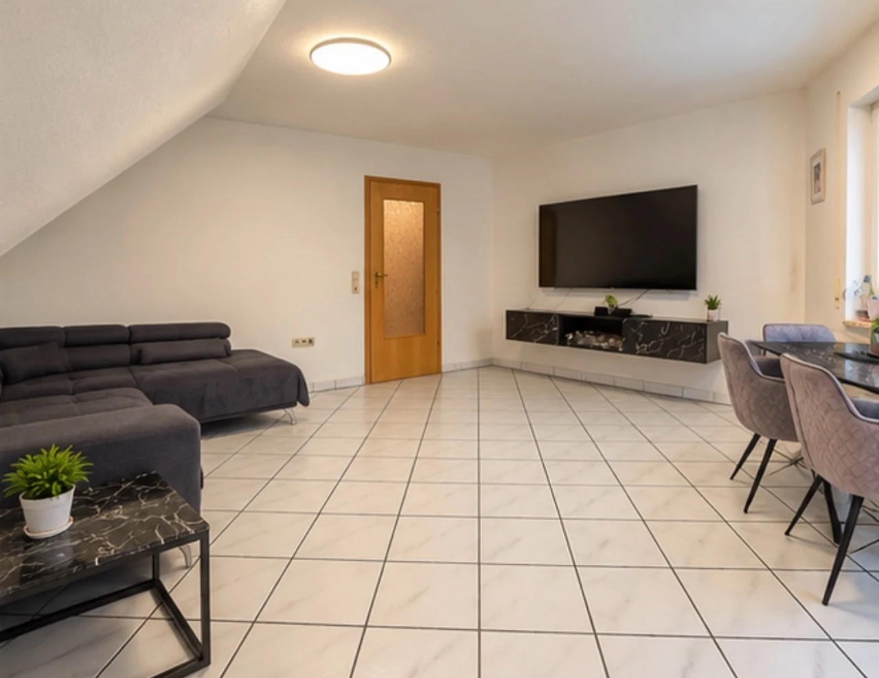Weiterer Blick in das Wohnzimmer mit Sofa, Essbereich und Dachschräge